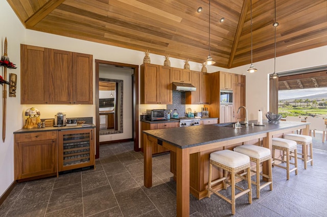 kitchen featuring wine cooler, dark countertops, a sink, wooden ceiling, and under cabinet range hood