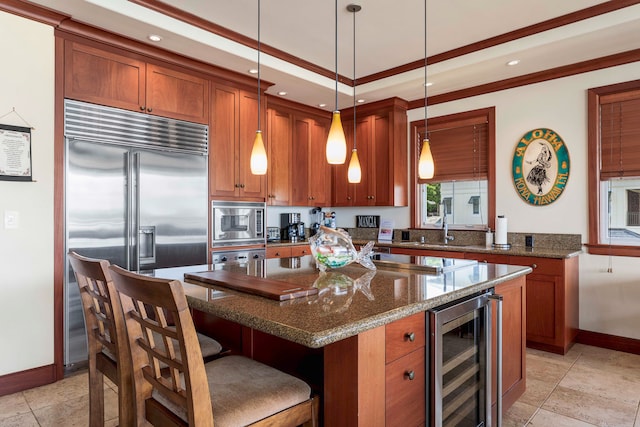 kitchen with pendant lighting, dark stone countertops, built in appliances, wine cooler, and a kitchen island