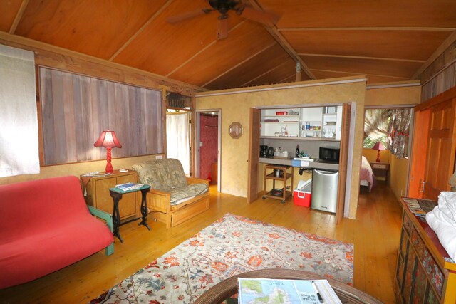 living room with ceiling fan, lofted ceiling, light hardwood / wood-style floors, and wood walls