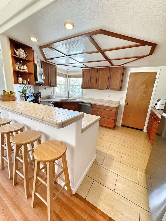 kitchen featuring tile counters, a breakfast bar, a textured ceiling, kitchen peninsula, and stainless steel appliances