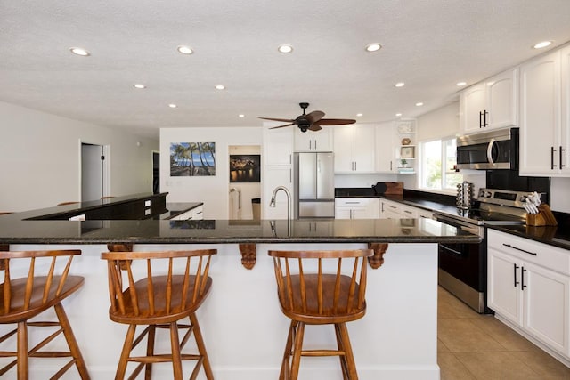 kitchen featuring light tile patterned flooring, appliances with stainless steel finishes, a breakfast bar area, and white cabinets