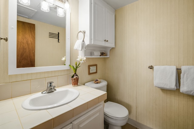 bathroom with vanity, toilet, and wooden walls