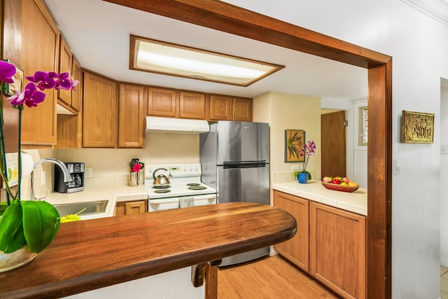 kitchen featuring light wood-type flooring, sink, stainless steel fridge, white range with electric stovetop, and tile counters