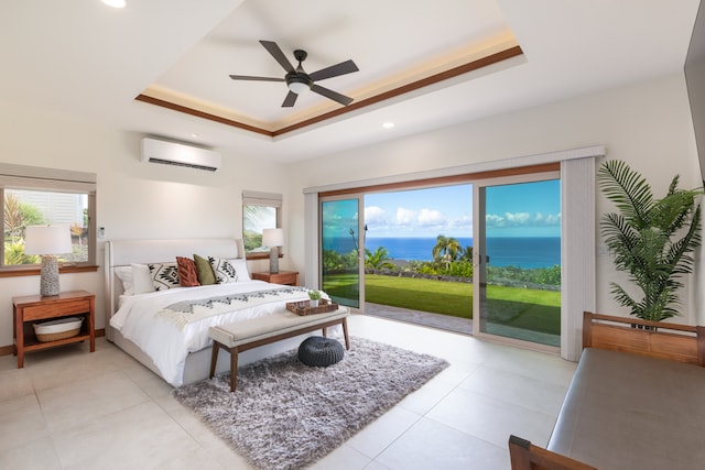 bedroom featuring a wall mounted AC, a tray ceiling, access to exterior, ceiling fan, and a water view