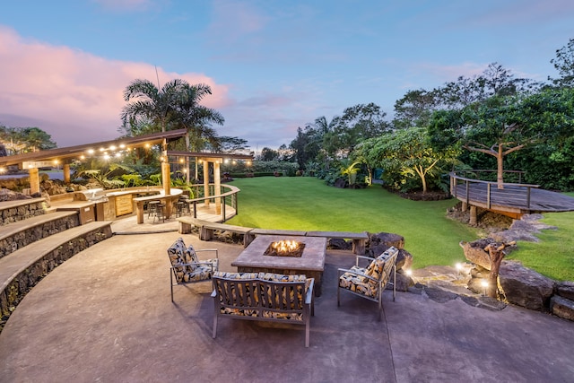 patio terrace at dusk with area for grilling, a yard, and a fire pit