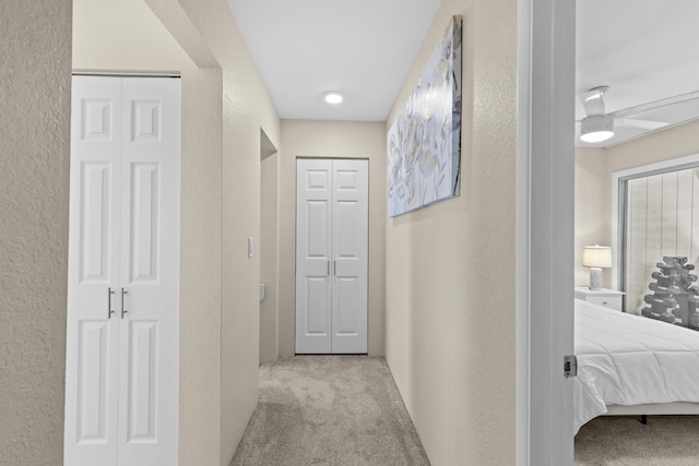 hallway with light carpet and a textured wall