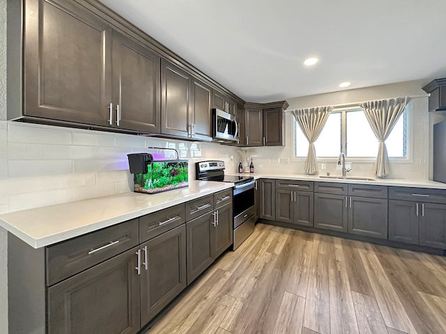 kitchen with appliances with stainless steel finishes, dark brown cabinets, sink, tasteful backsplash, and light wood-type flooring