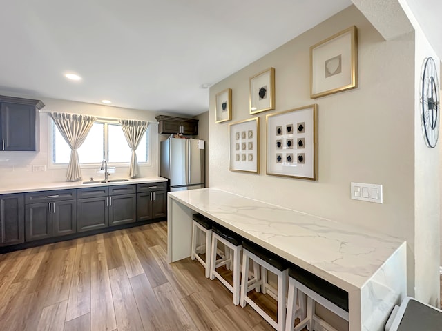 kitchen featuring sink, light wood-type flooring, dark brown cabinetry, light stone counters, and stainless steel refrigerator