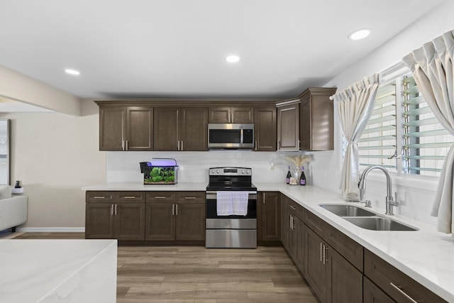 kitchen with appliances with stainless steel finishes, a sink, dark brown cabinetry, and light wood-style floors