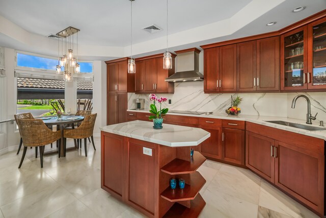 kitchen featuring a notable chandelier, pendant lighting, wall chimney exhaust hood, sink, and a kitchen island