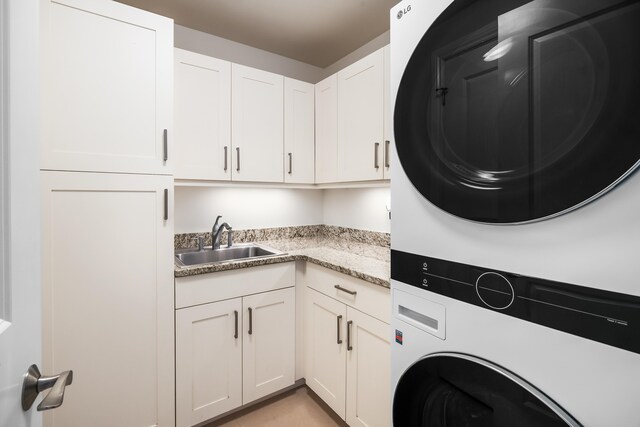 laundry area featuring cabinets, sink, and stacked washer / dryer