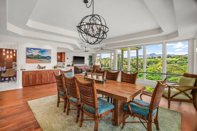 dining area with ceiling fan with notable chandelier, a raised ceiling, and light hardwood / wood-style flooring