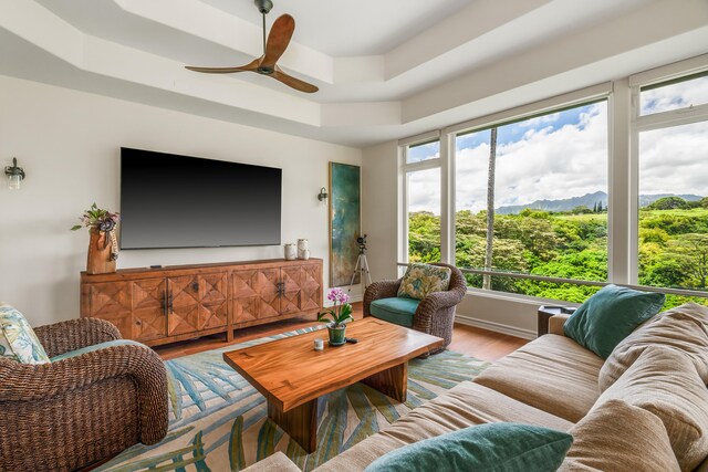 living room featuring wood-type flooring, ceiling fan, and a tray ceiling