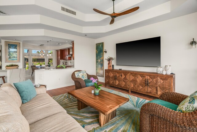 living room with ceiling fan, a tray ceiling, and wood-type flooring