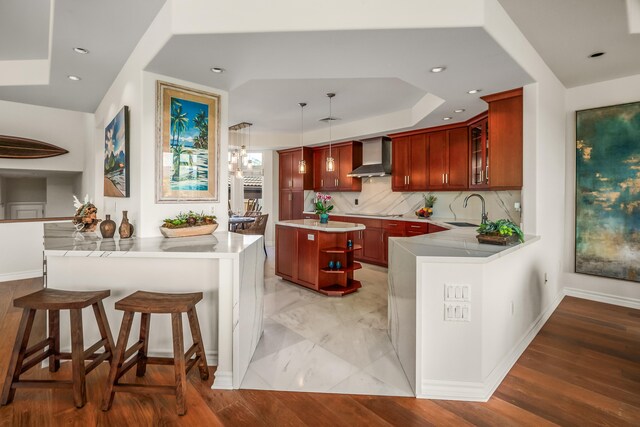 kitchen with wall chimney range hood, decorative backsplash, pendant lighting, sink, and kitchen peninsula