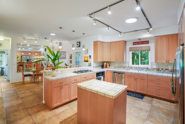 kitchen with tasteful backsplash, stainless steel appliances, a center island, tile counters, and kitchen peninsula