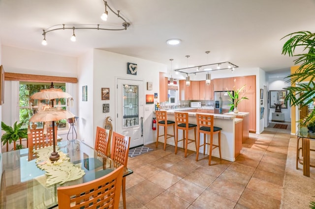 kitchen with kitchen peninsula, stainless steel refrigerator with ice dispenser, a breakfast bar, light tile patterned floors, and track lighting