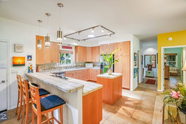 kitchen featuring tasteful backsplash, stainless steel fridge, kitchen peninsula, rail lighting, and a center island