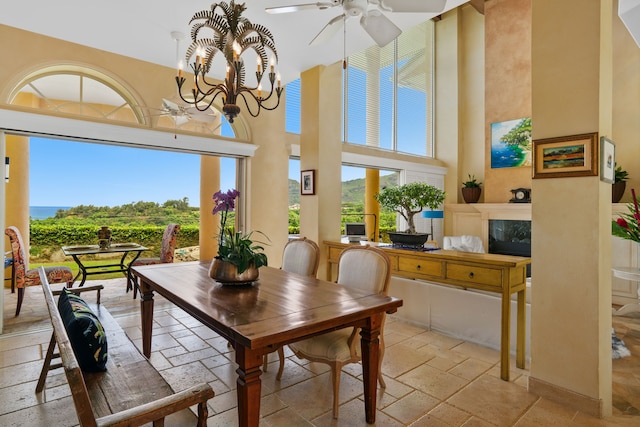 dining space with a high end fireplace, ceiling fan with notable chandelier, light tile patterned floors, and a high ceiling