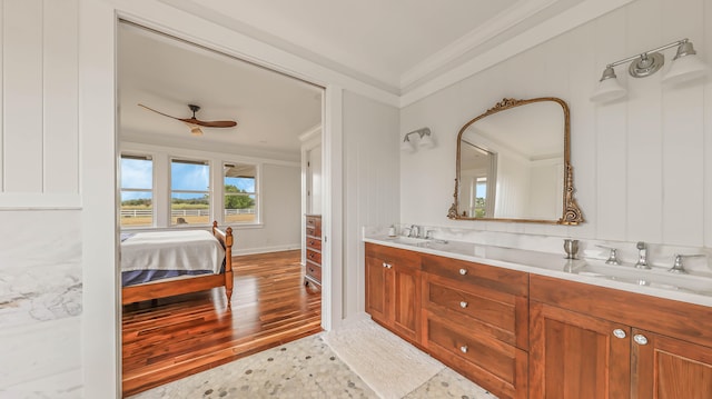 ensuite bathroom with wood finished floors, crown molding, a sink, and double vanity