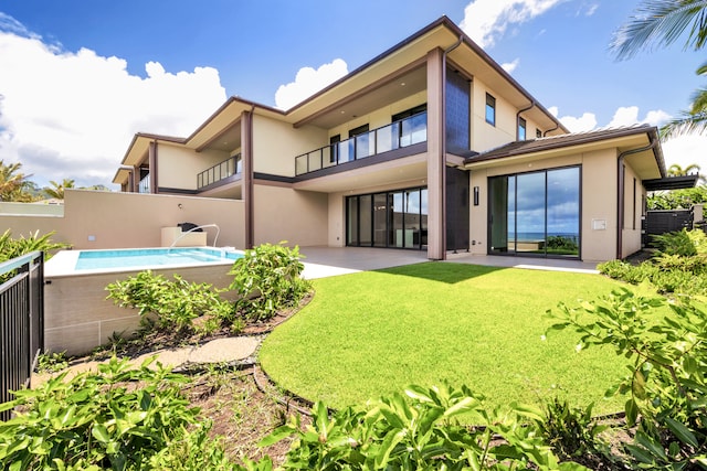 rear view of property featuring a patio, a balcony, and a lawn