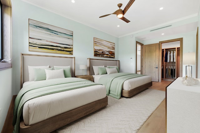 bedroom featuring a walk in closet, a closet, light hardwood / wood-style floors, ceiling fan, and crown molding