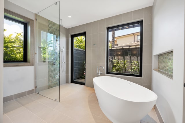 bathroom with a wealth of natural light, tile patterned flooring, shower with separate bathtub, and tile walls