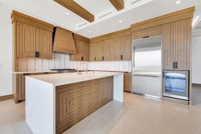 kitchen featuring wine cooler, a kitchen island with sink, premium range hood, light tile patterned floors, and stainless steel appliances