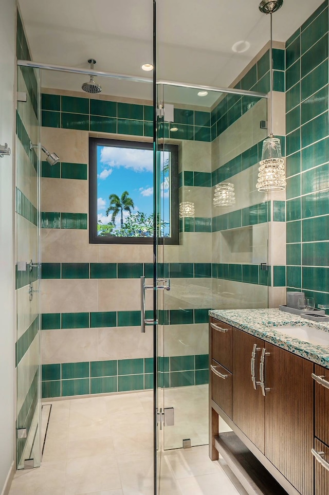 bathroom with tile patterned flooring, a shower with door, vanity, and tile walls