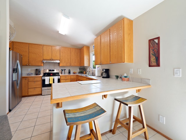 kitchen featuring a breakfast bar area, kitchen peninsula, stainless steel appliances, and vaulted ceiling