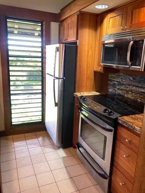 kitchen with dark stone countertops, a wealth of natural light, light tile patterned floors, and stainless steel appliances