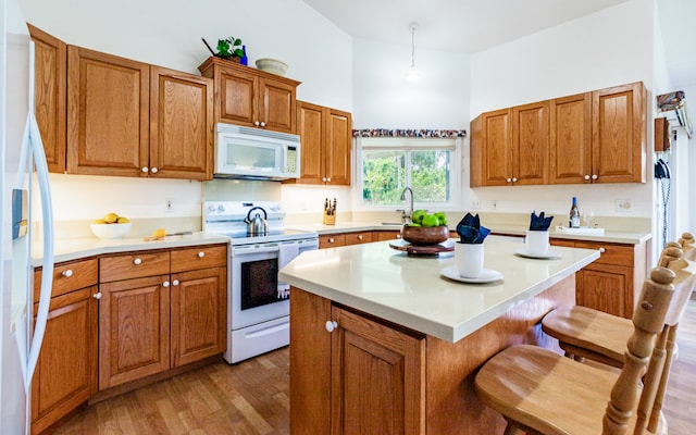 kitchen featuring pendant lighting, white appliances, a kitchen island, a kitchen breakfast bar, and hardwood / wood-style floors