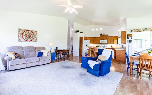 living room featuring light hardwood / wood-style flooring, ceiling fan, high vaulted ceiling, and sink