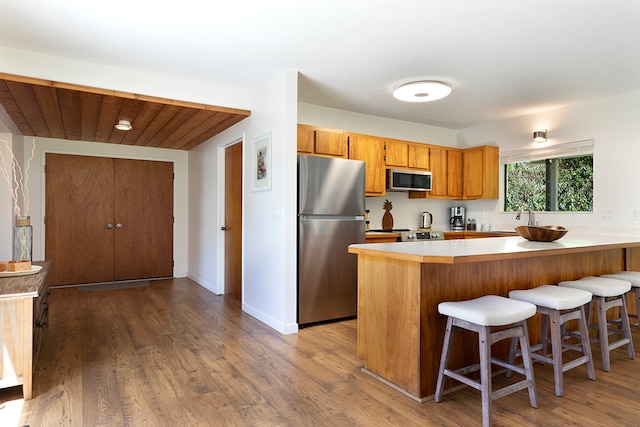 kitchen with a kitchen breakfast bar, stainless steel appliances, light hardwood / wood-style floors, and kitchen peninsula