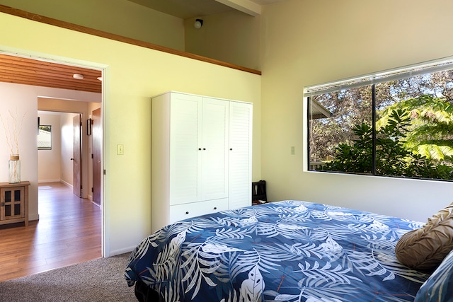 bedroom with beamed ceiling, a closet, wood-type flooring, and a towering ceiling