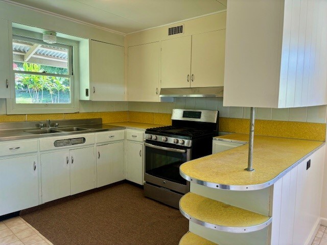 kitchen featuring kitchen peninsula, white cabinets, dark tile patterned flooring, sink, and stainless steel range with gas cooktop