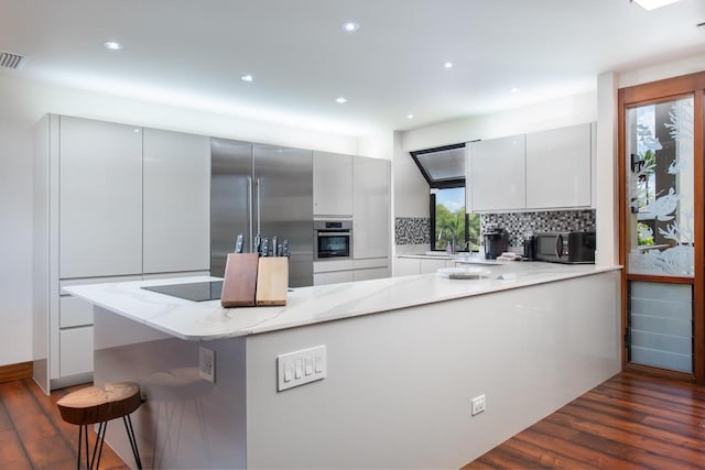 kitchen with dark wood-style flooring, tasteful backsplash, modern cabinets, light stone countertops, and black appliances