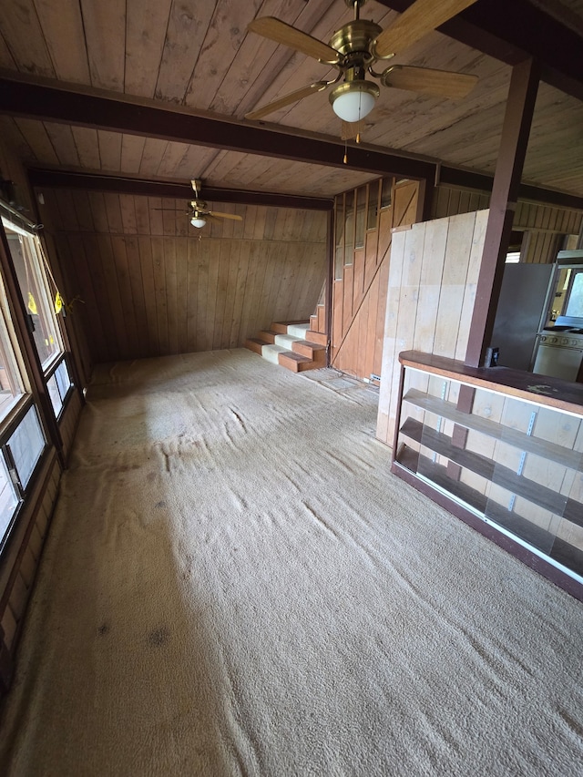 unfurnished living room with carpet floors, wood ceiling, ceiling fan, and wood walls