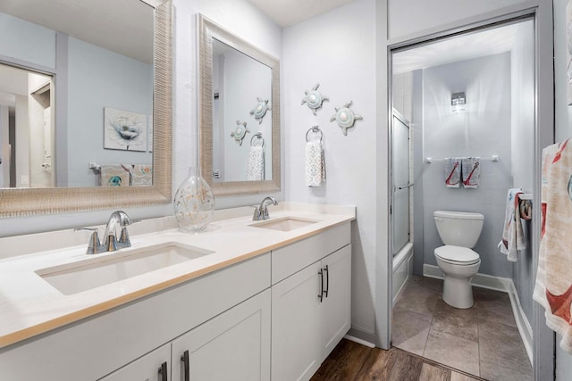 full bathroom with hardwood / wood-style flooring, enclosed tub / shower combo, double sink vanity, and toilet