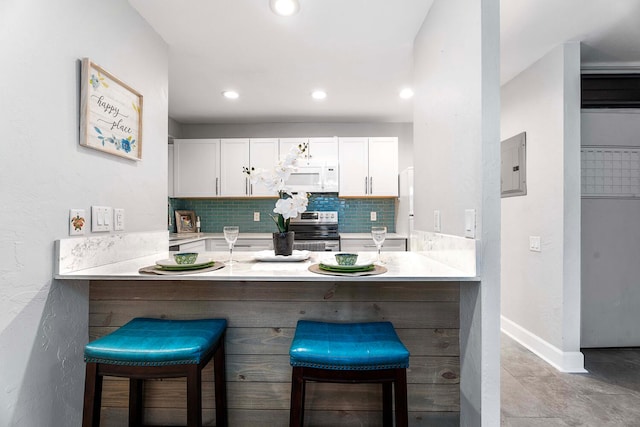 kitchen featuring a kitchen bar, stainless steel electric range oven, kitchen peninsula, and white cabinets