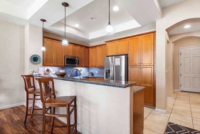 kitchen with appliances with stainless steel finishes, light hardwood / wood-style floors, tasteful backsplash, a tray ceiling, and pendant lighting