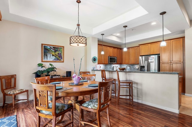 dining area with a tray ceiling, dark hardwood / wood-style flooring, and sink