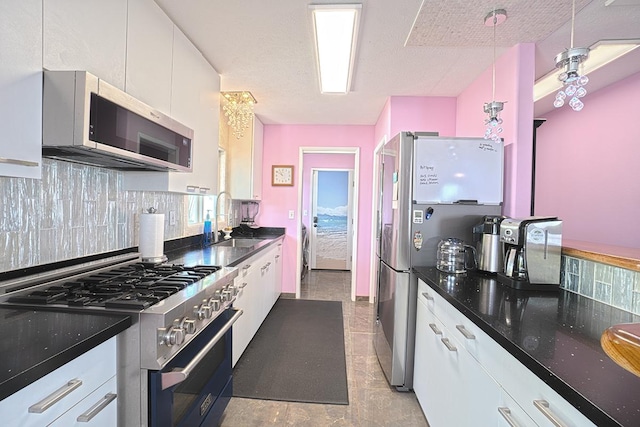 kitchen featuring stainless steel appliances, backsplash, white cabinets, a sink, and dark stone counters