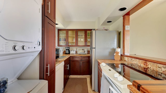 kitchen featuring stacked washer / dryer, light tile patterned flooring, and white appliances