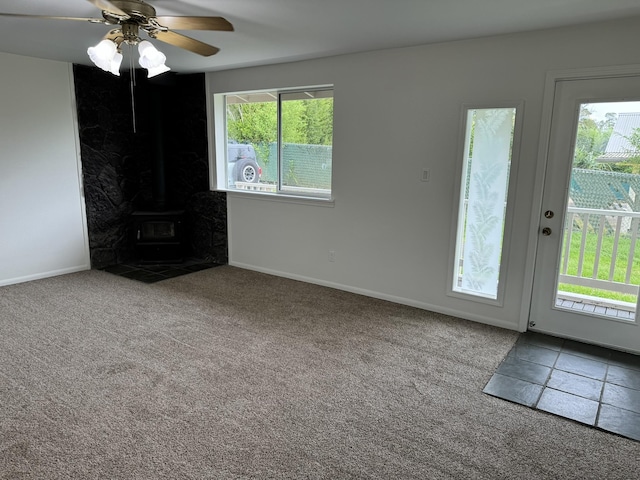 unfurnished living room featuring carpet floors, ceiling fan, and a wood stove