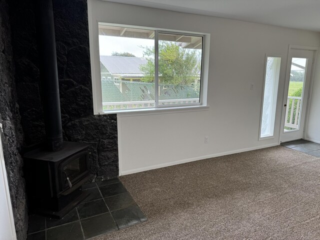 unfurnished living room with a wood stove, a wealth of natural light, and carpet flooring