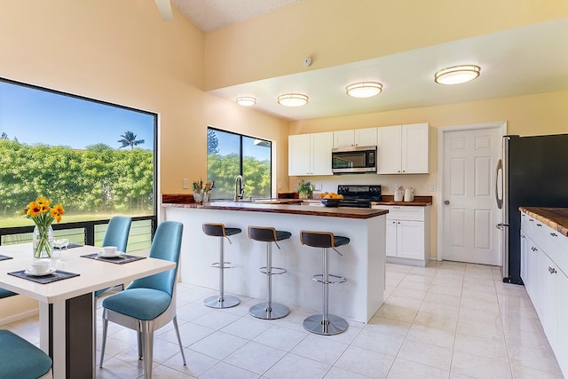 kitchen featuring a kitchen breakfast bar, light tile patterned flooring, stainless steel appliances, and white cabinets