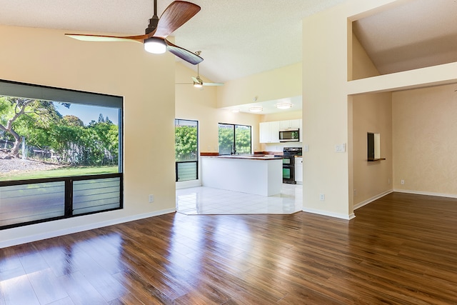 unfurnished living room with a textured ceiling, wood-type flooring, ceiling fan, and high vaulted ceiling