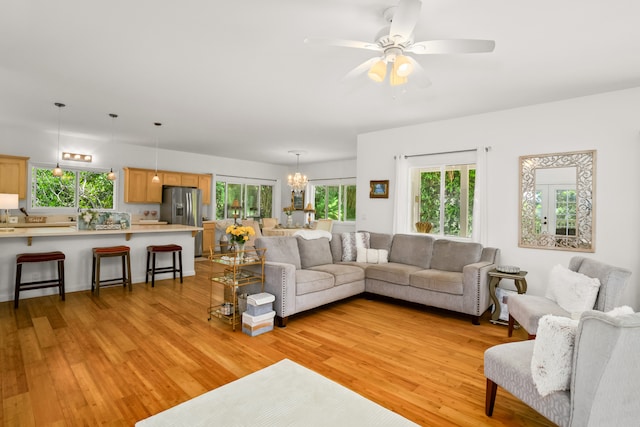 living room with ceiling fan with notable chandelier and light hardwood / wood-style floors