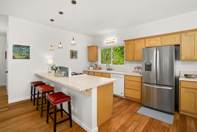 kitchen with a breakfast bar area, white dishwasher, sink, light hardwood / wood-style floors, and stainless steel fridge